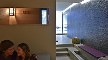 Un espace spa moderne doté d’un mur en bois, d’un mur en pierre et d’un coin salon avec des marches menant à une piscine.