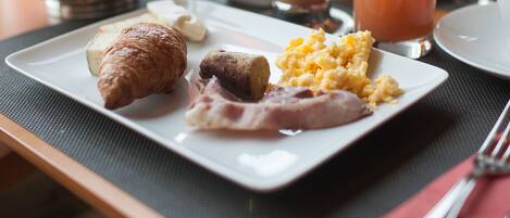 A breakfast tray with croissants, scrambled eggs, bacon, and juice.