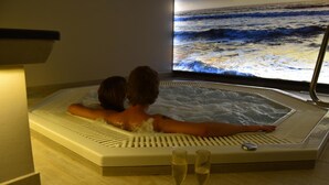 Un couple se détend dans un jacuzzi, tandis qu’un grand écran diffuse des images de vagues océaniques.