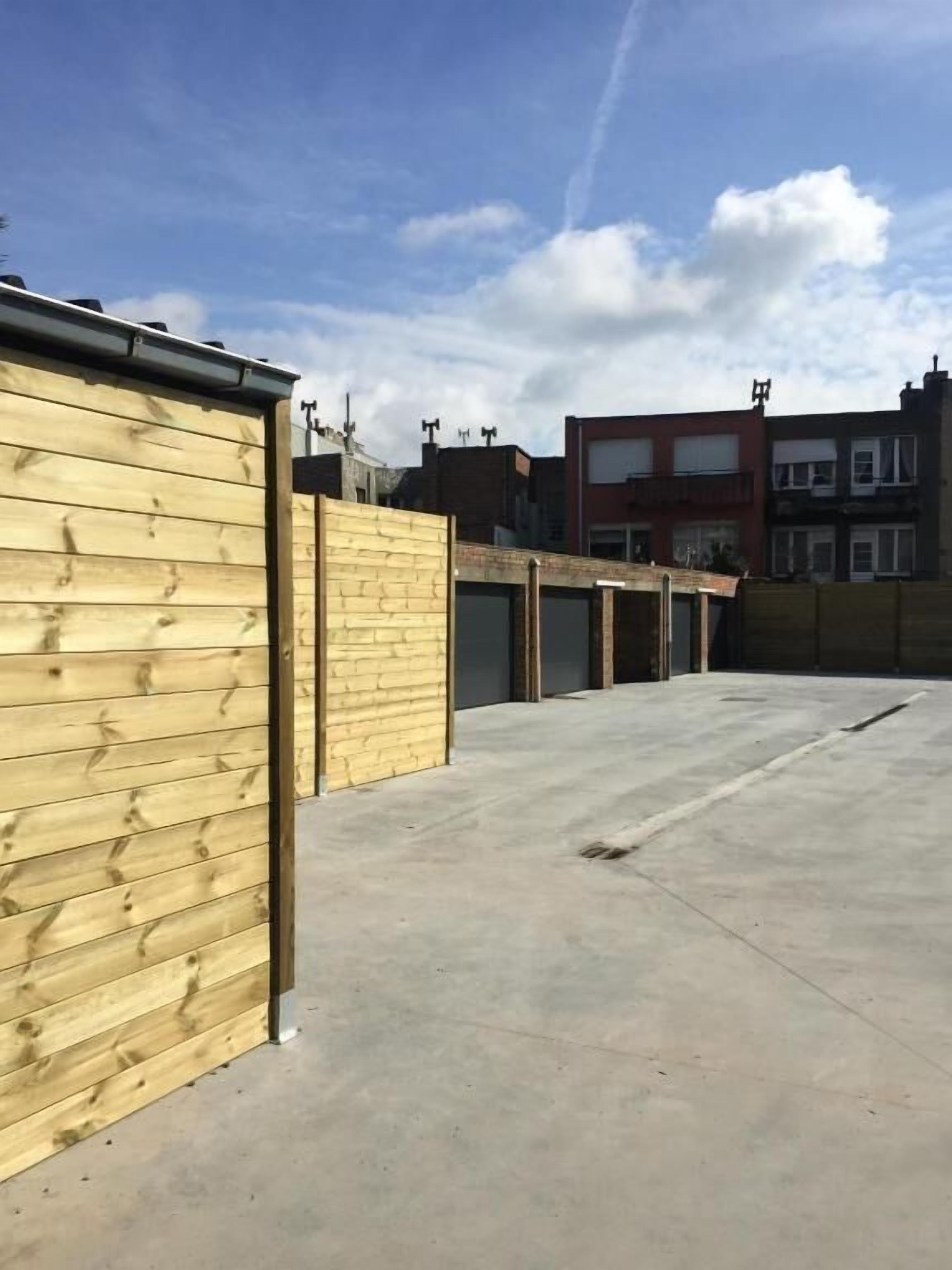 A rooftop with a concrete floor, wooden fencing, and a row of buildings in the background.