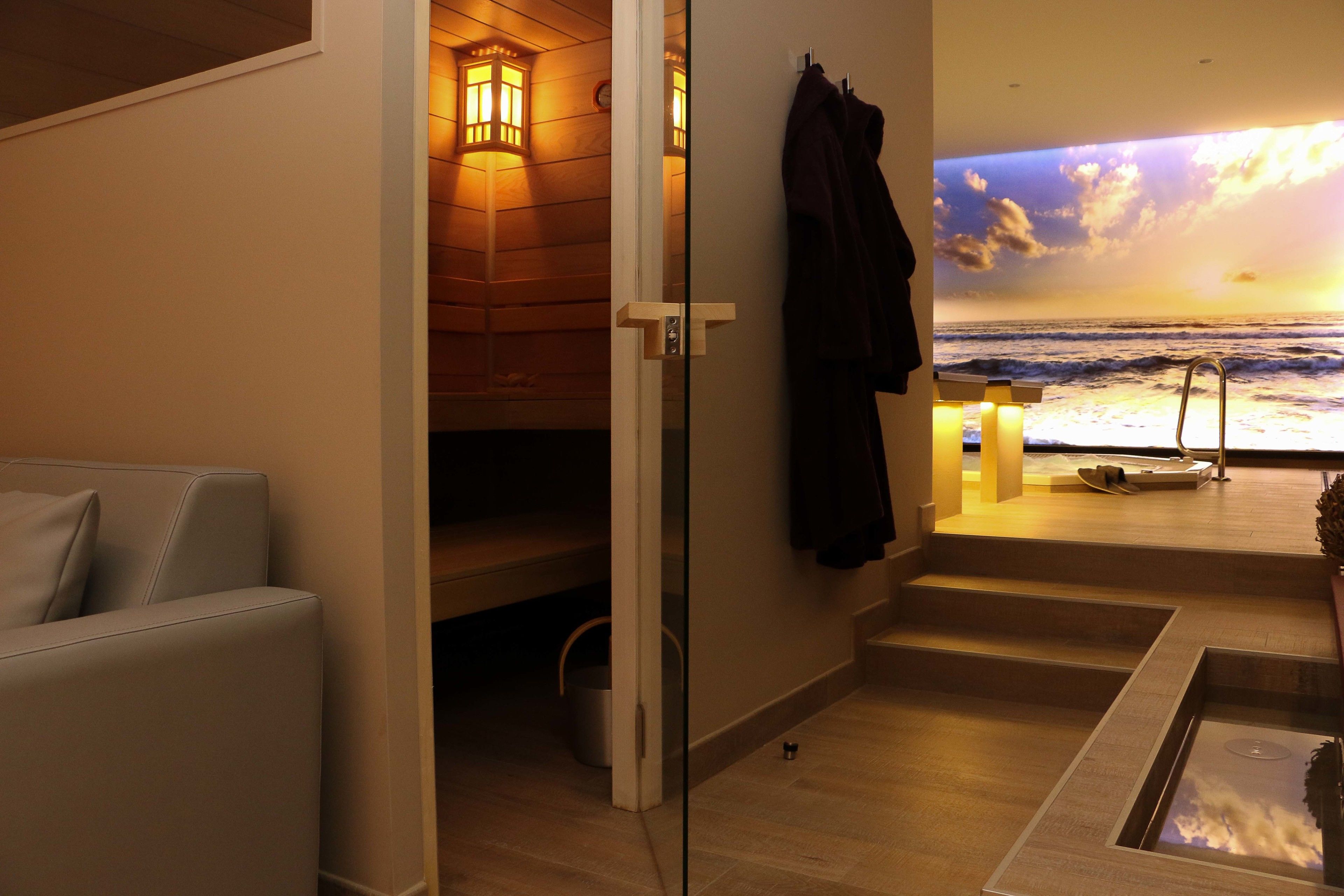 Una stanza spa con parete in legno, lettino da massaggio e vista sull'oceano al tramonto.