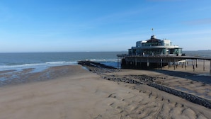 Un bâtiment situé en bord de mer, doté d’une façade en verre, d’une structure en forme de dôme sur le toit et d’une jetée qui s’avance dans l’océan.