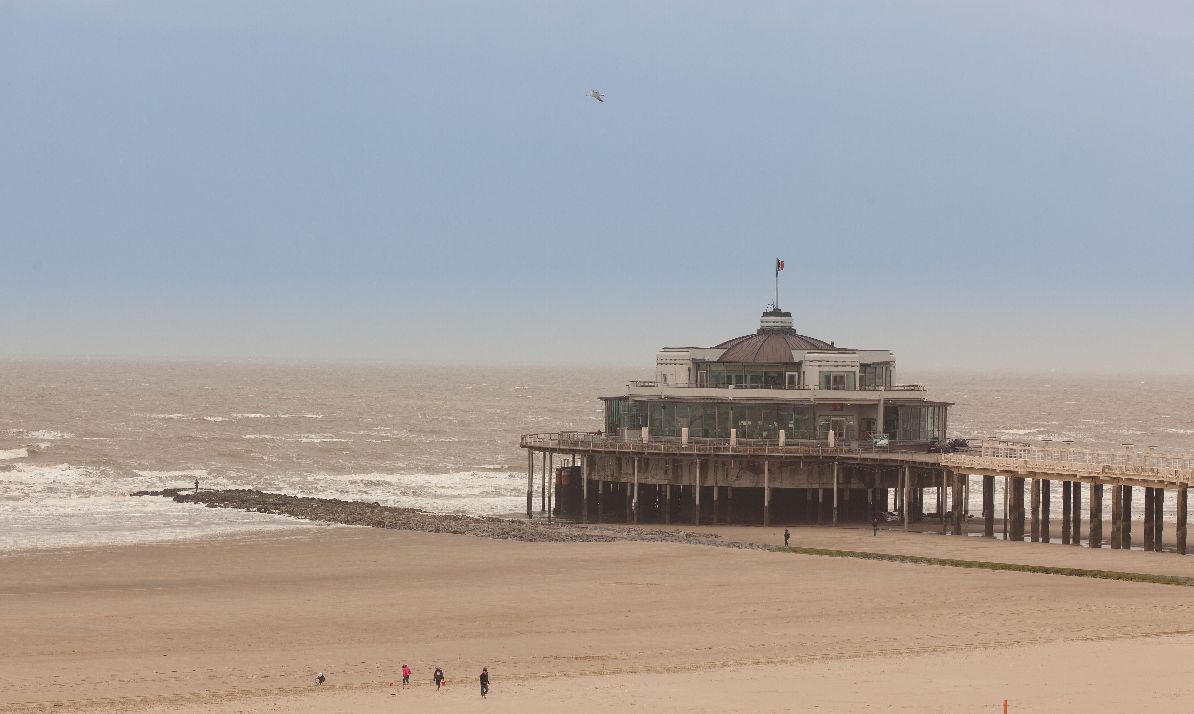 Um píer à beira-mar com uma torre de observação, uma praia de areia e o oceano.