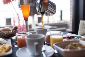Een ontbijtsetting met een koffiemachine die koffie in een kop schenkt, een fruitschaal en diverse ontbijtartikelen op een tafel.