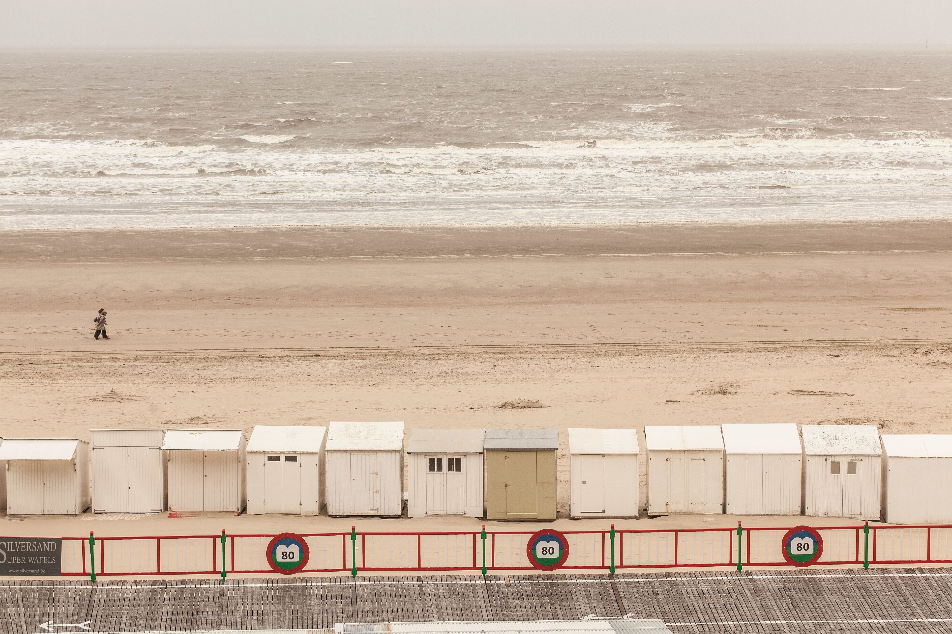 A beach with a row of white beach huts and a speed limit sign of 80.