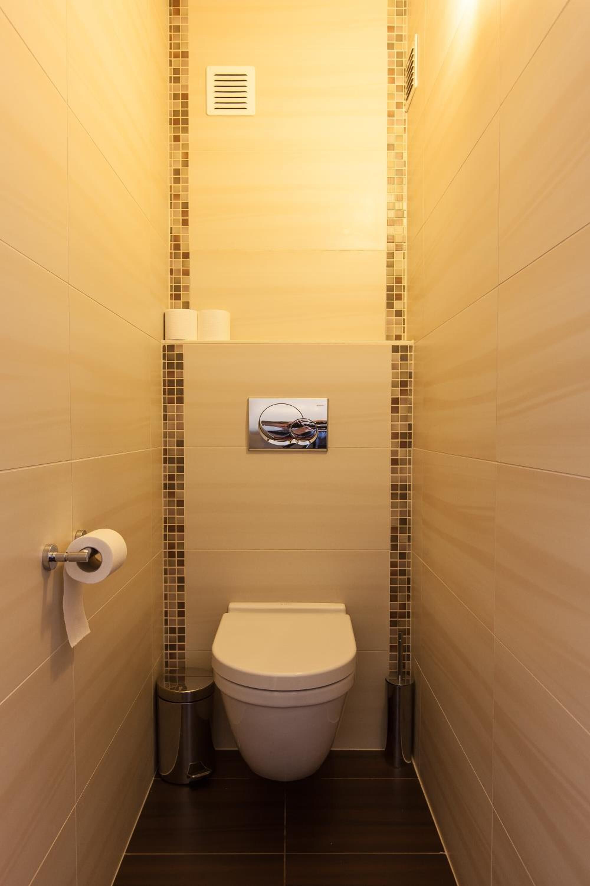 A narrow bathroom with a toilet, a trash can, and a small picture frame on the wall.