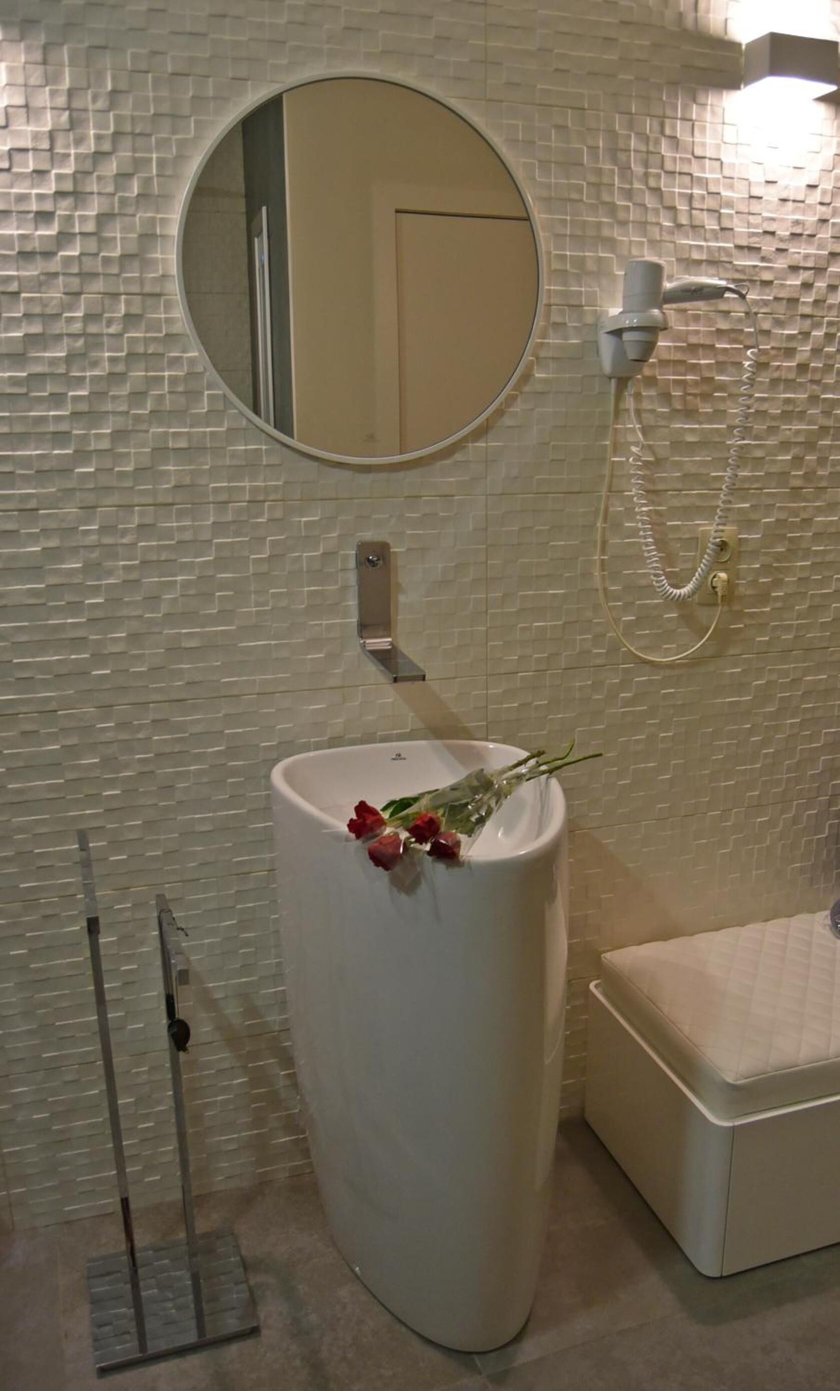 Une salle de bain avec un grand lavabo blanc, un miroir rond, une douchette et des toilettes.