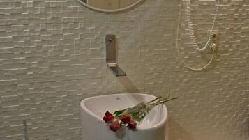 Une salle de bain avec un grand lavabo blanc, un miroir rond, une douchette et des toilettes.