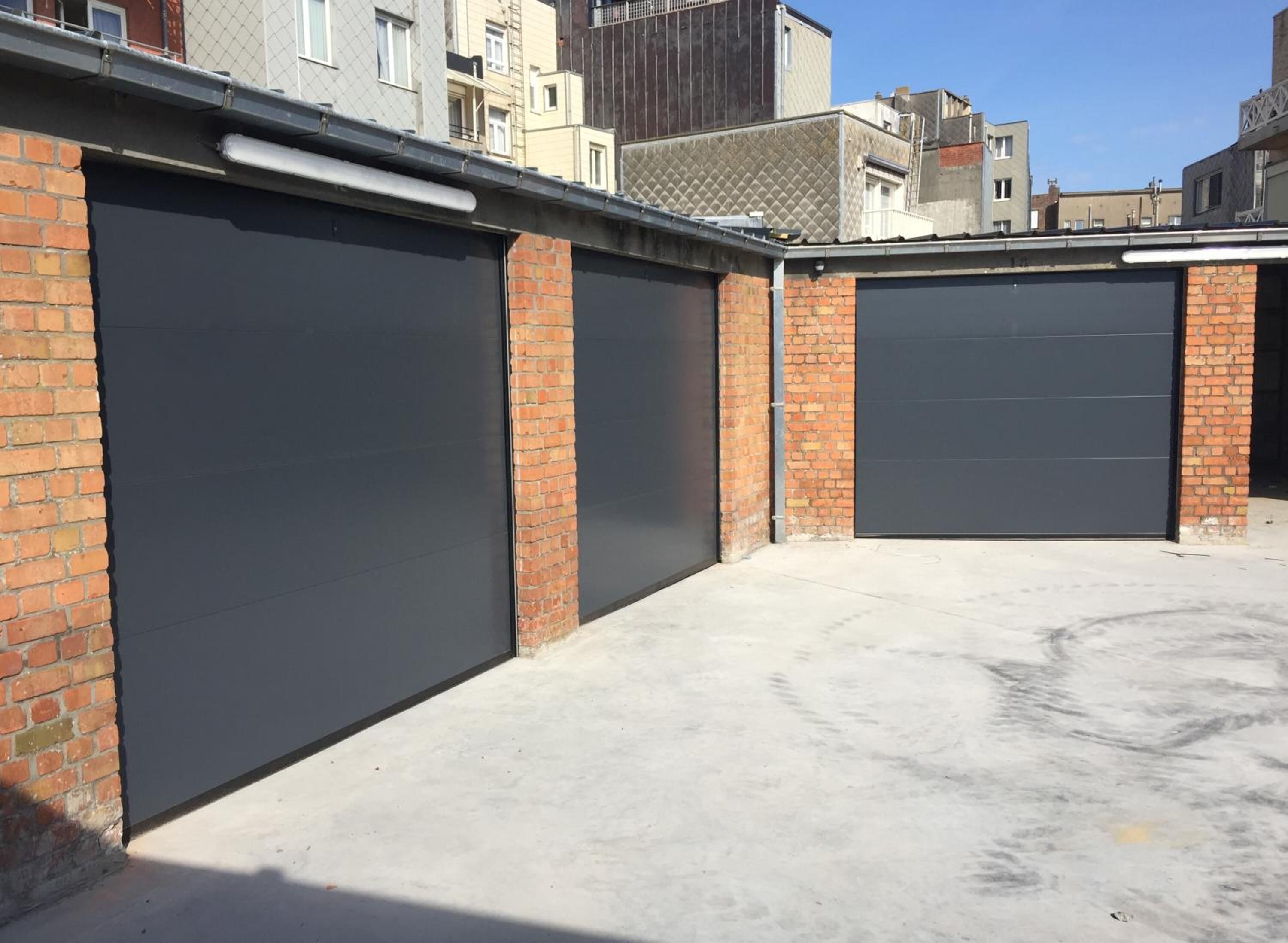 A parking garage with three large, dark-colored garage doors, brick walls, and a concrete floor.