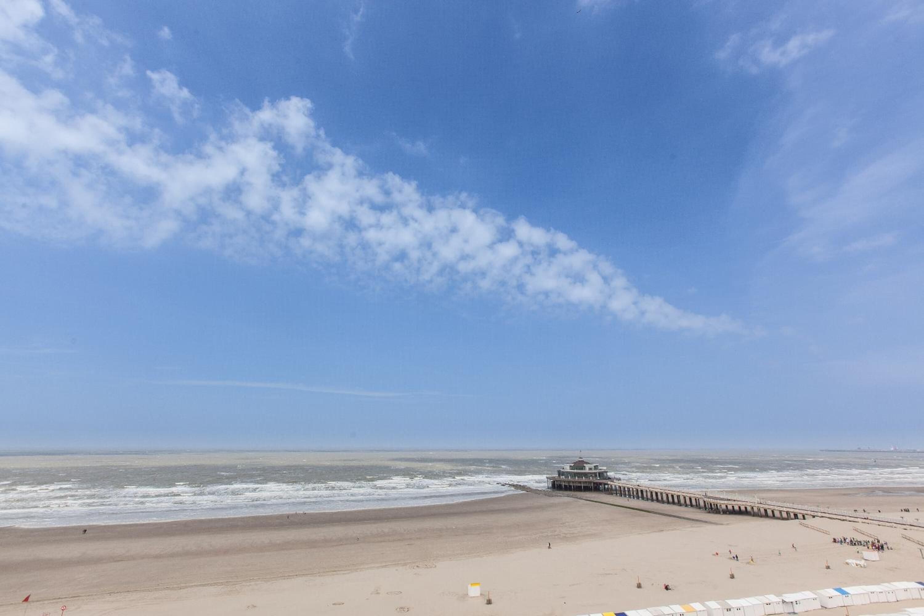 A beach with a pier extending into the ocean, a sandy beach, and a clear sky.