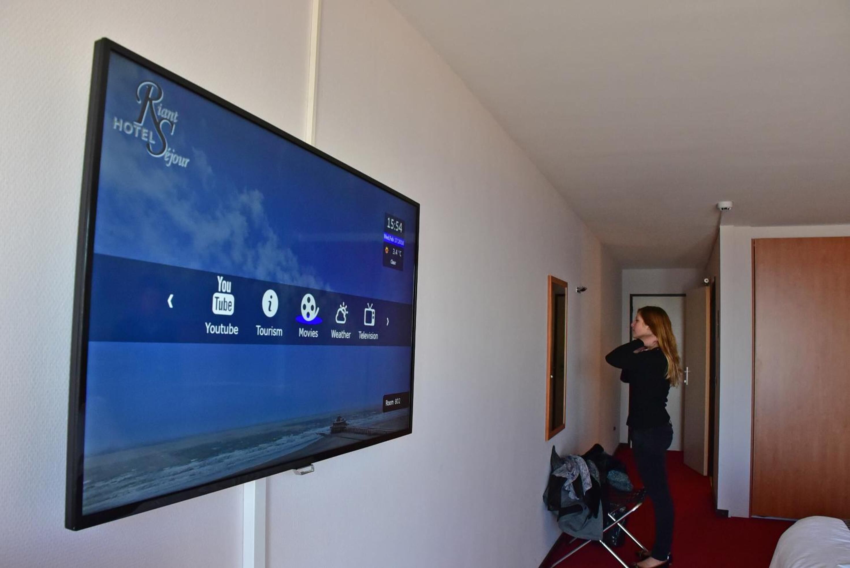 A hotel room with a large flat-screen TV mounted on the wall displaying a weather app.