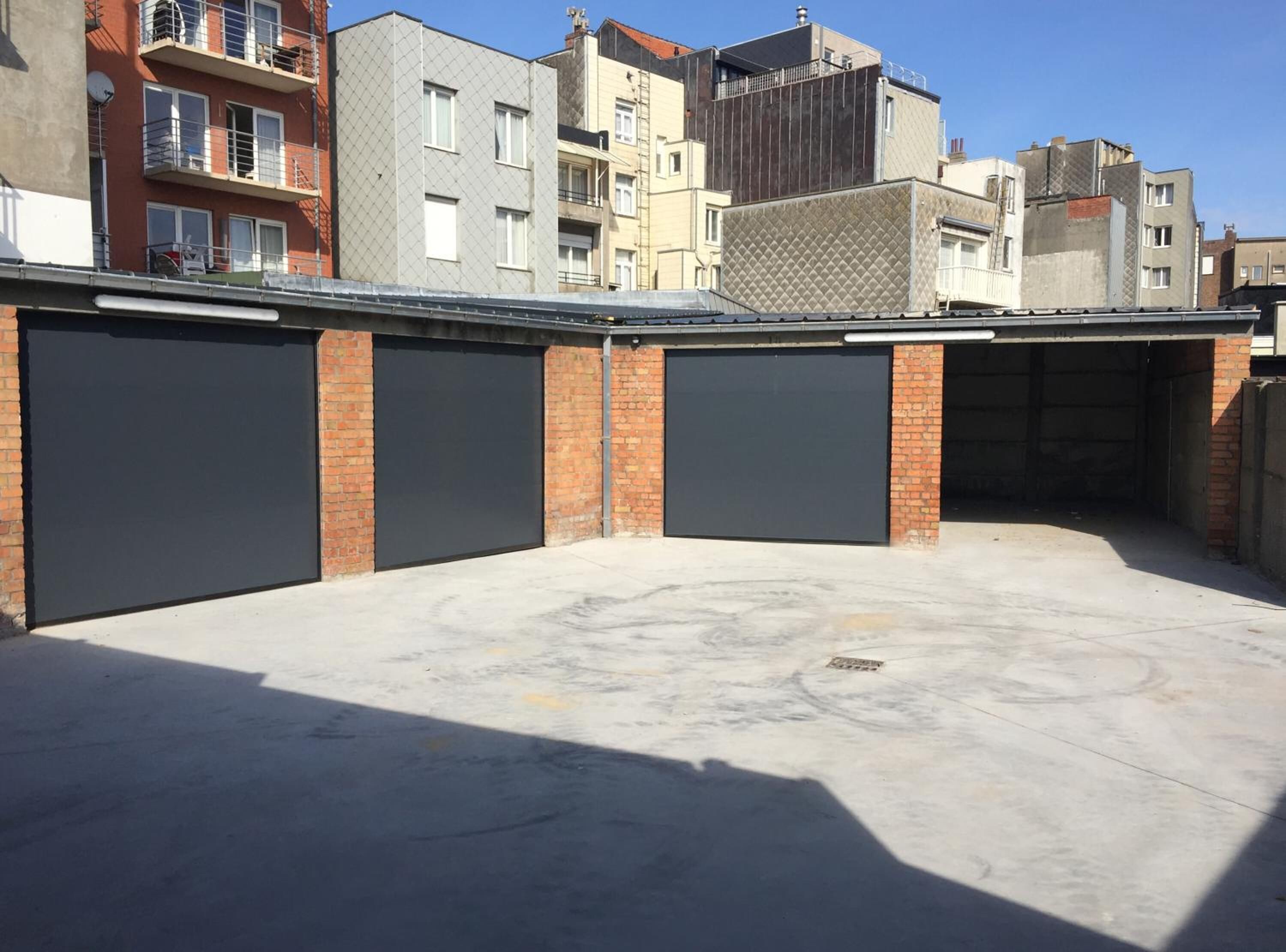 Ein Parkplatz mit drei geschlossenen Garagentoren, umgeben von mehrstöckigen Gebäuden.