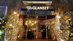 A modern building entrance with the sign "GLANSIT" above the doors. There are two illuminated decorative structures on either side of the entrance. - Glansit Akihabara Comfort Capsule Hotel (Tokyo)