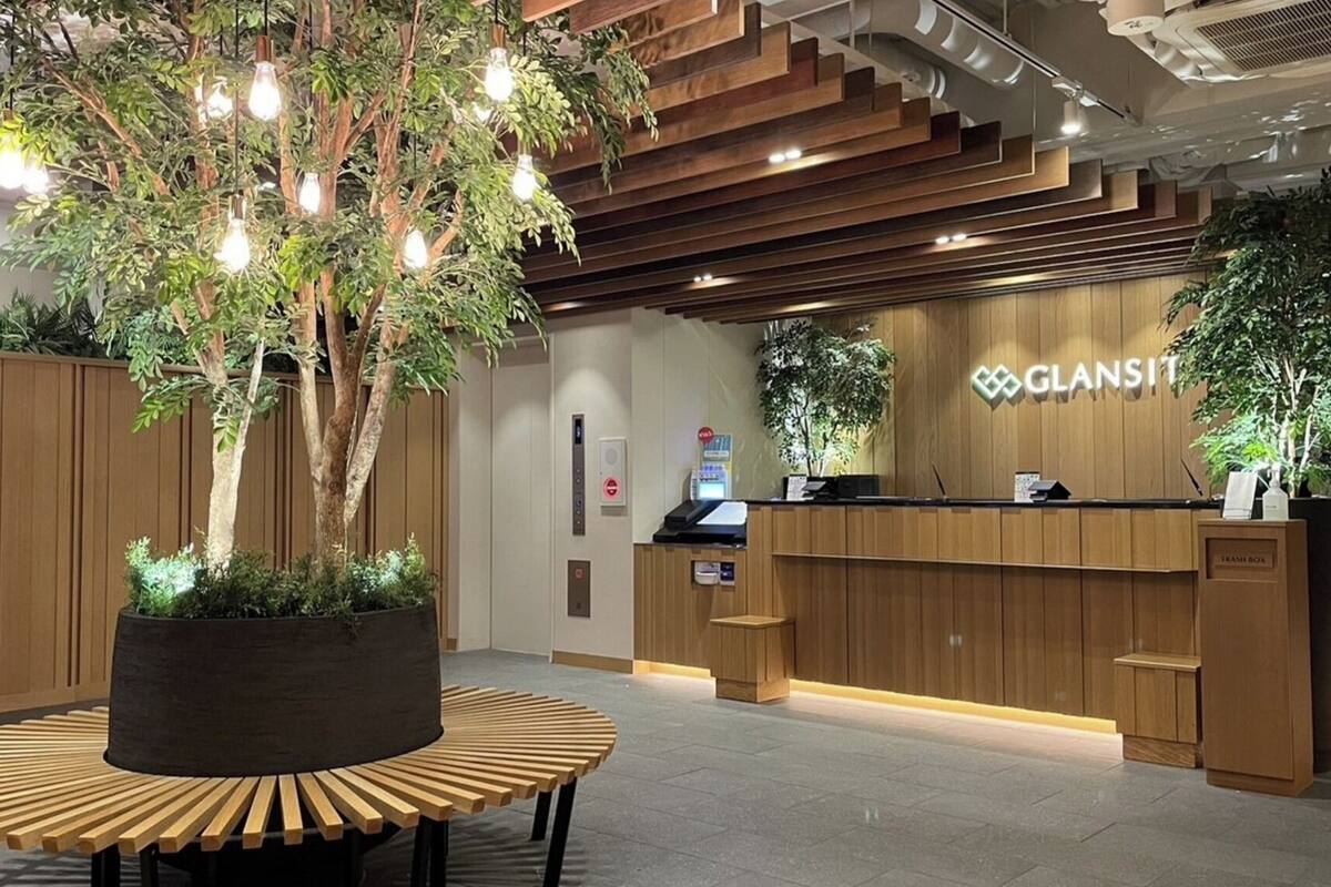 Un área de recepción con un mostrador de madera, una planta grande en maceta y un mostrador de recepción con un letrero que dice 'GLANST'.