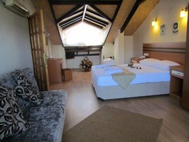 Un dormitorio acogedor con una cama grande, un sofá, un escritorio y una pequeña mesa con un jarrón de flores.