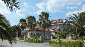 A two-story building with a red roof and multiple windows, surrounded by palm trees and a gravel driveway. - Dalyan Palmiye Resort (Ortaca)