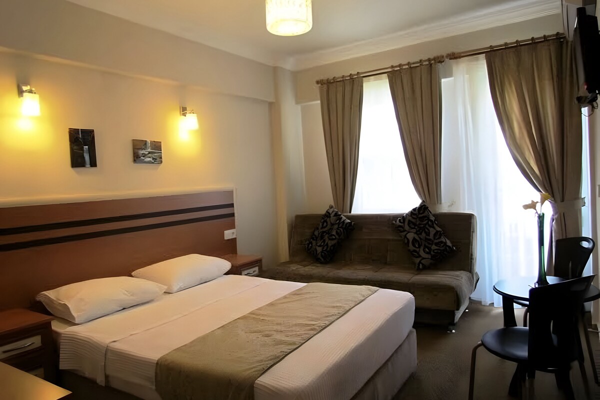 Une chambre d’hôtel avec un lit, un canapé, une chaise, un bureau et une fenêtre avec des rideaux.