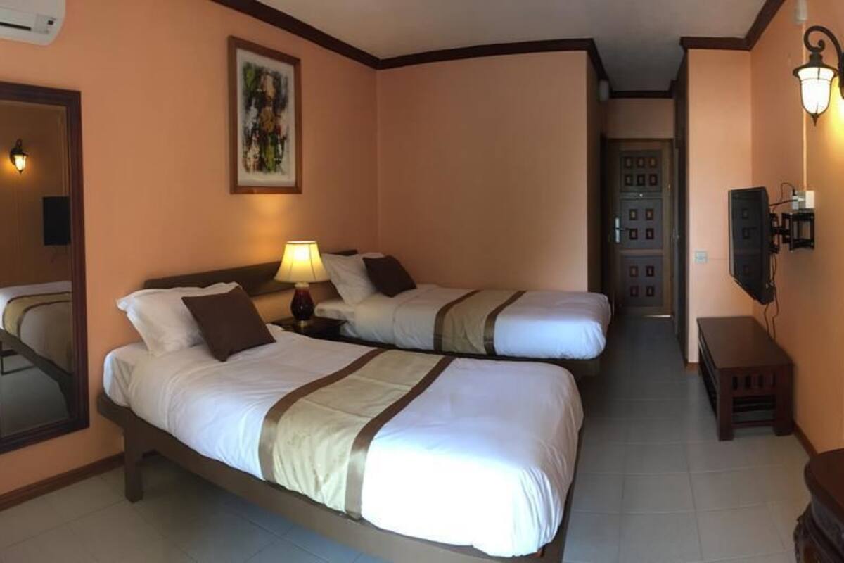 A hotel room with two beds, a mirror, a painting, a lamp, and a TV.