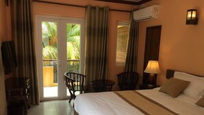 A hotel room with a bed, two chairs, a table, an air conditioning unit, and a view of palm trees through the glass door. - Ocean Lake Tourist Residence (Grand-Baie)