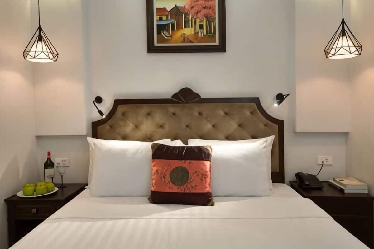 A neatly made bed with a tufted headboard, a single decorative pillow, and a framed picture above.