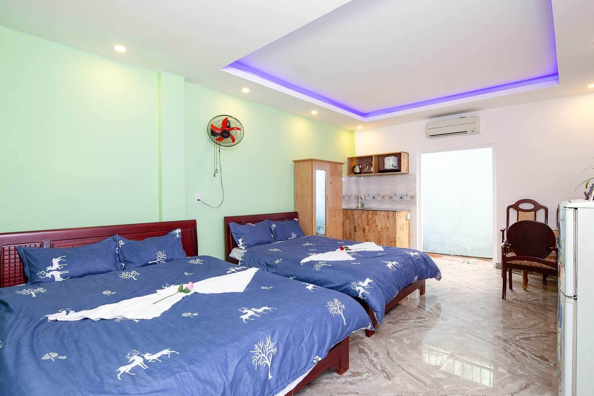 Une chambre d’hôtel avec deux lits, un ventilateur de plafond, un appareil de climatisation et une armoire en bois.