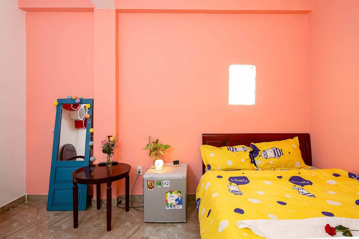 Une chambre à coucher avec un lit, une petite table, une chaise, un réfrigérateur et un miroir.