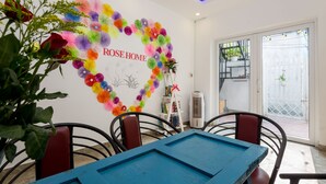 A dining area with a blue table and chairs, a wall mural with a heart shape and the text "ROSE HOME", and a view of a balcony with plants. - Rose Garden Homestay Da Nang 2 - Hostel (Da Nang)