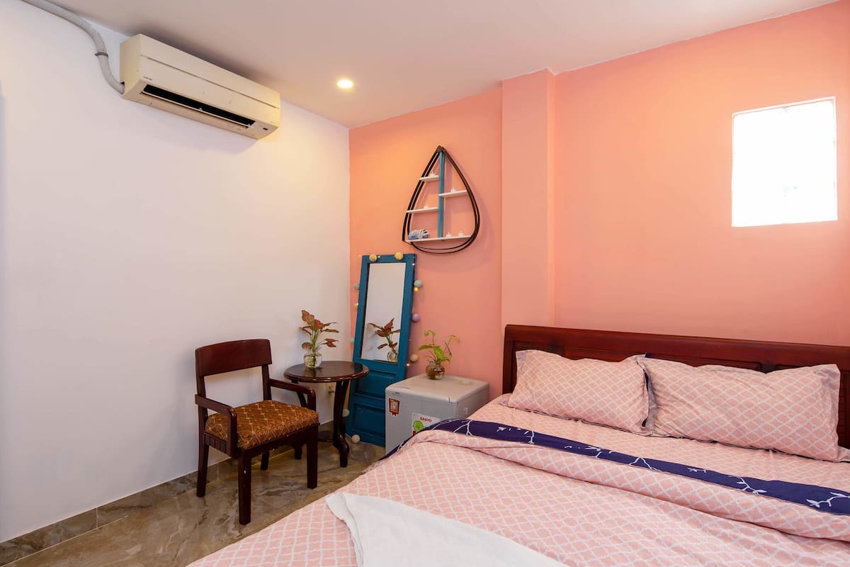 Une chambre à coucher comprenant un lit, une chaise, une petite table, un miroir et un appareil de climatisation.