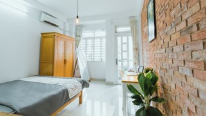 A bedroom with a bed, a wooden wardrobe, a desk with a chair, a potted plant, and a brick wall. - Urban House Saigon 2 (Ho Chi Minh City)