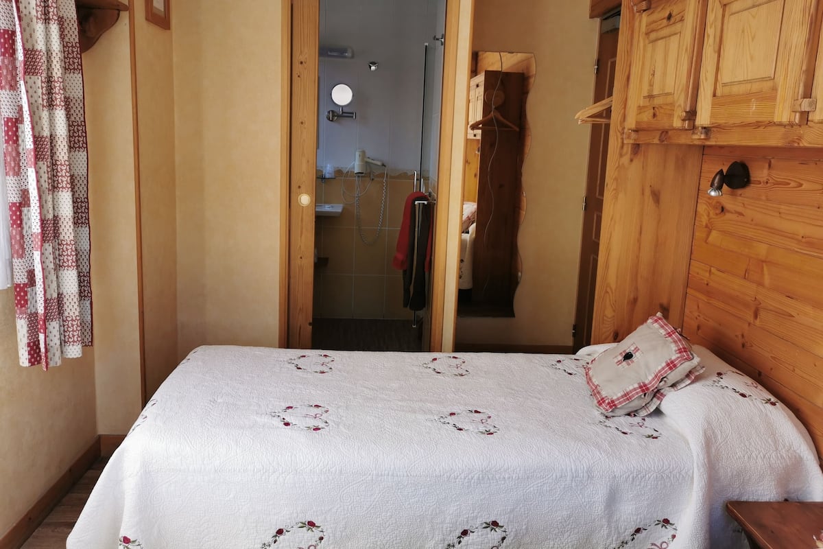 Una camera da letto con un letto, un armadio in legno e un bagno visibile attraverso una porta aperta.