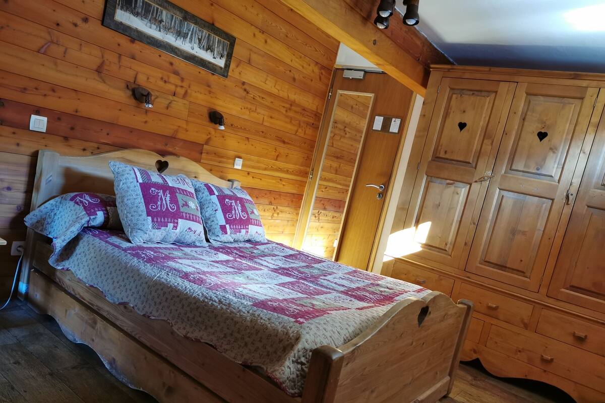 Un letto di legno con una coperta, un armadio in legno e una porta in una stanza dalle pareti di legno.