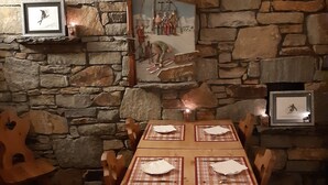 Una mesa de madera para comer, con individuales y cubiertos, flanqueada por paredes de piedra y sillas de madera.