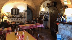 Un restaurant avec des arches en briques, des nappes à carreaux et des bouteilles de vin exposées sur des étagères.