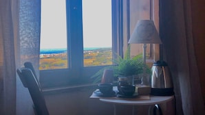 Une pièce avec vue sur un paysage, visible par une fenêtre, comprenant une table avec une lampe, une chaise et un lit.