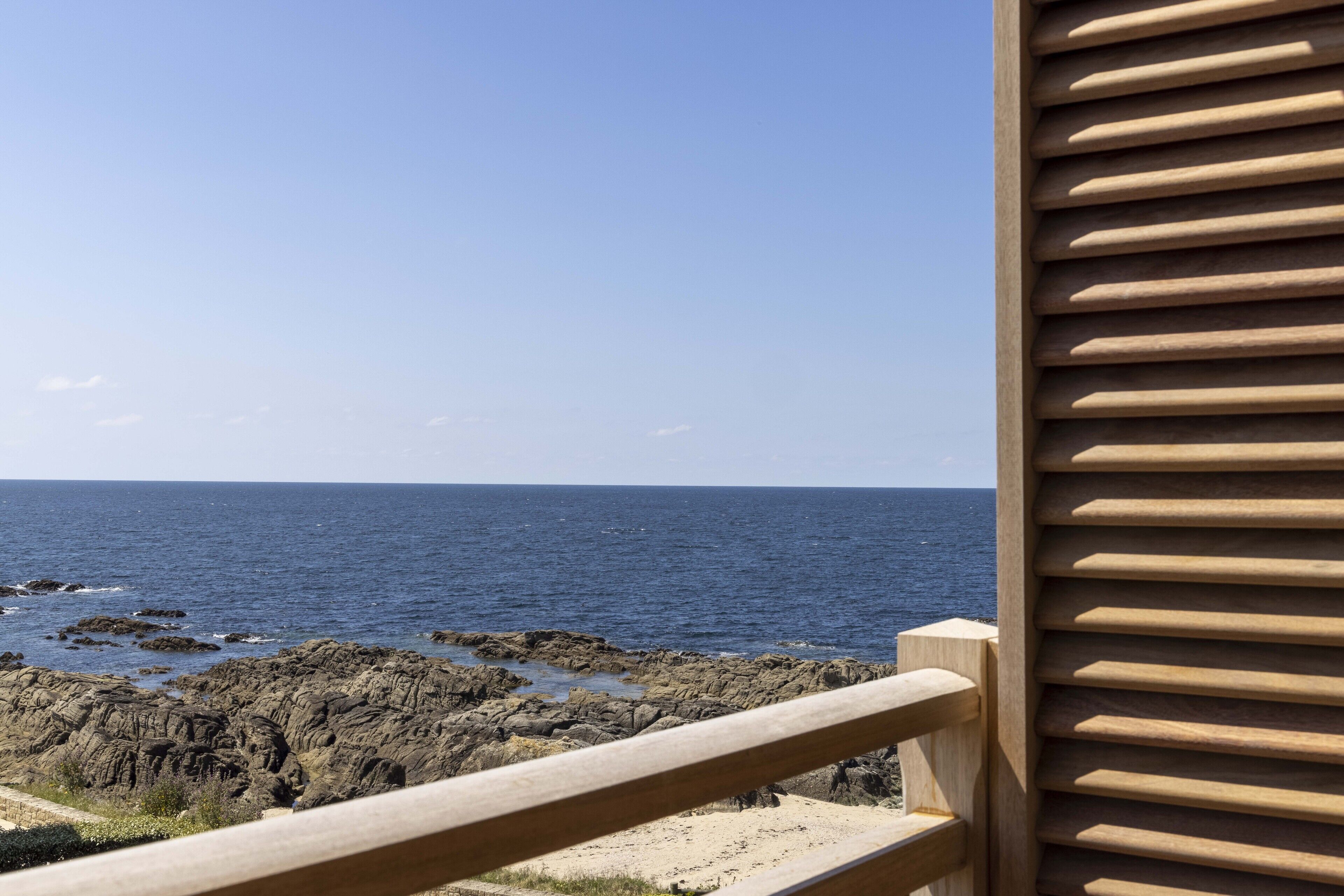 A view of the ocean from a balcony with a wooden railing.