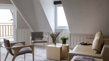 Um quarto de loft moderno com teto inclinado, uma janela grande, um sofá, uma poltrona, uma mesa pequena e um vaso com flores.