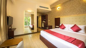 A hotel room with a large bed, a TV, a desk, and a view of the outdoors. - Samudra Mysore (Mysore)