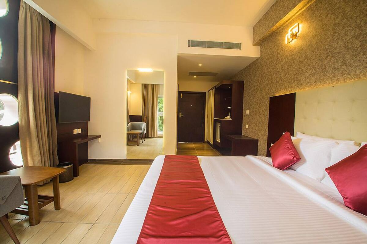 Quarto de hotel com uma cama grande, uma escrivaninha, uma cadeira, uma televisão e vista para o corredor.