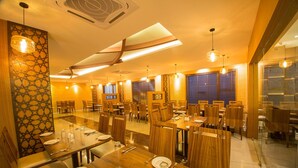 A spacious restaurant with multiple dining tables and chairs, warm lighting, and decorative wall panels. - Samudra Mysore (Mysore)