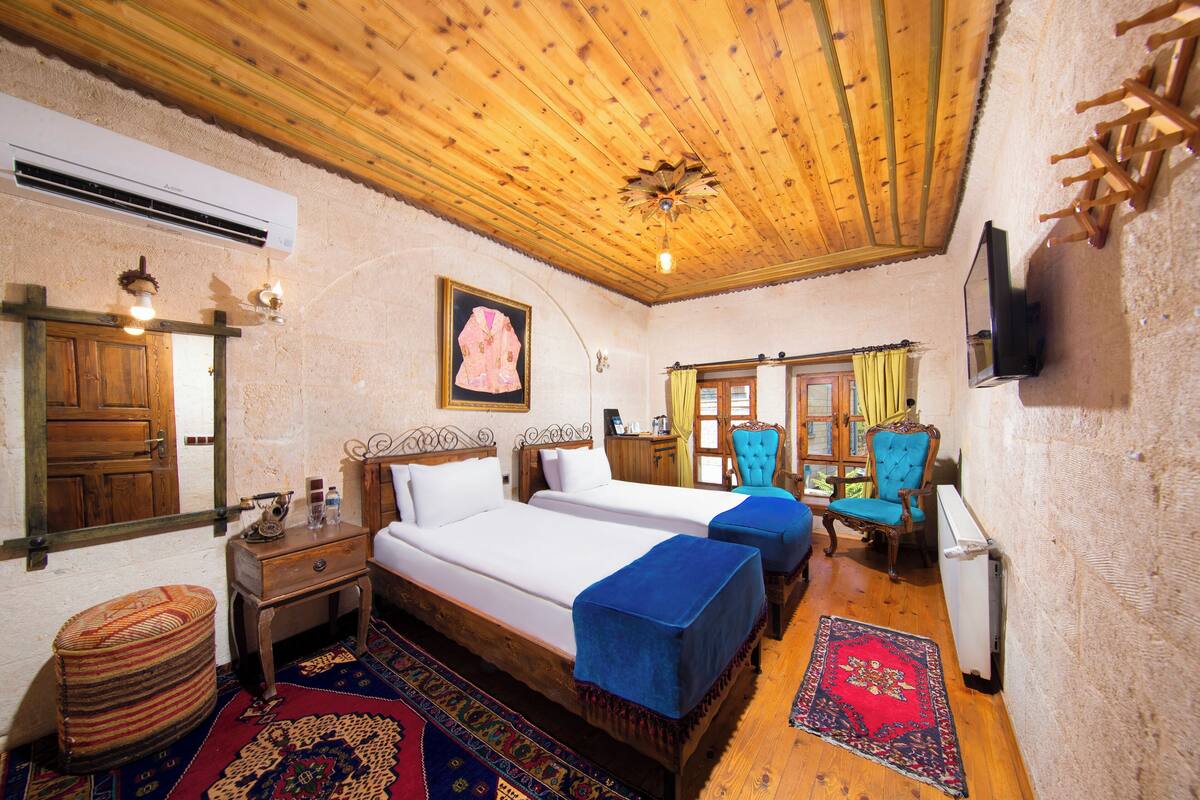 Una habitación tradicional con techo de madera, dos camas, un televisor y una alfombra estampada.