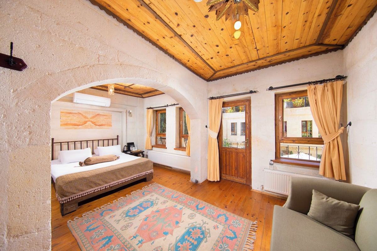 Un dormitorio con cama, sofá, alfombra estampada y vigas de madera en el techo.