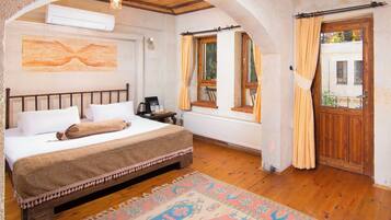 Un dormitorio con una cama grande, suelo de madera, alfombra estampada y una ventana con cortinas.