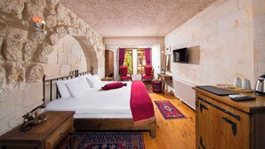 A bedroom with a stone wall, wooden bed, red curtains, a television, and a desk with a kettle. - Aja Cappadocia Hotel - Special Class  (Ürgüp)