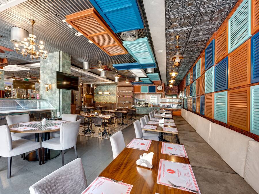A restaurant with a long counter, multiple tables, and chairs. There are ceiling fans and a TV mounted on the wall.