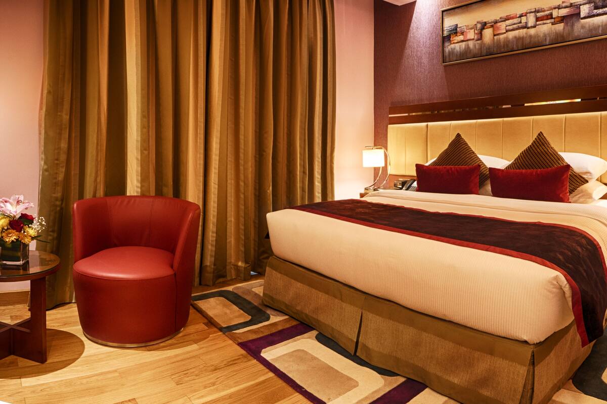 Ein Hotelzimmer mit einem großen Bett, einem roten Sessel, einem Nachttisch mit einer Lampe und einem Gemälde an der Wand.