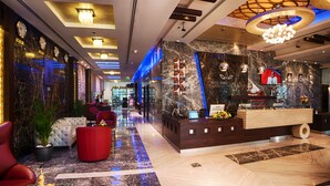 Een hotel lobby met een receptiebalie, een zithoek en een grote kroonluchter.