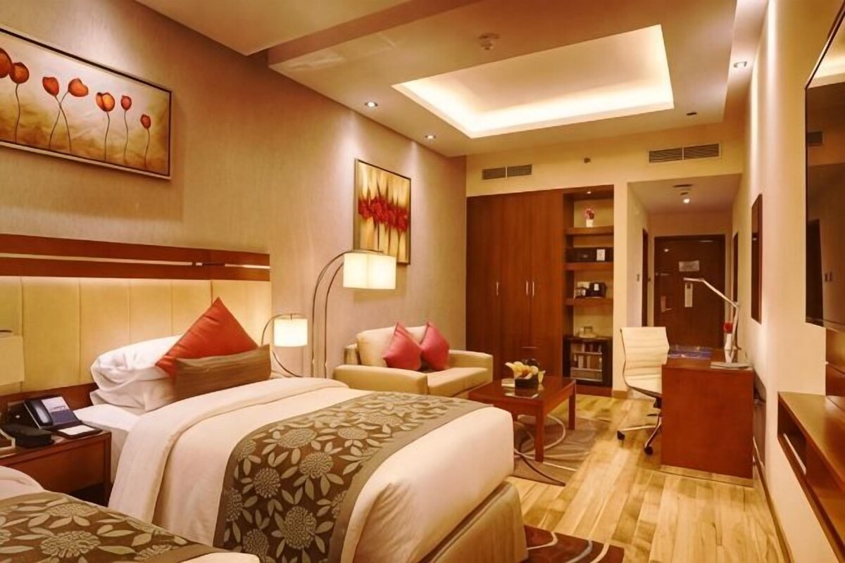 Une chambre d’hôtel avec un lit, un bureau, une chaise, un canapé, une lampe et un tableau au mur.