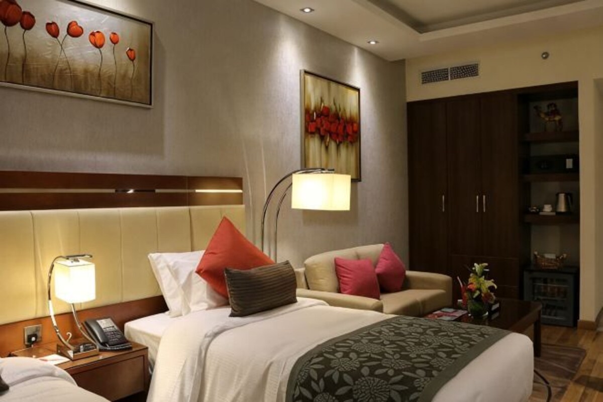 Een hotelkamer met een bed, nachtkastje, lamp, stoel en een kledingkast.