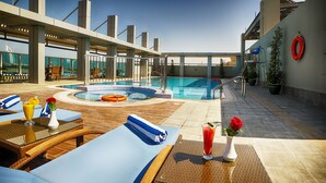 Een dakterras met een zwembad, ligbedden, een jacuzzi en uitzicht op de stadshemel.