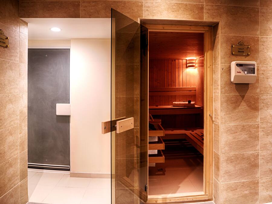 Un sauna avec des bancs en bois et une porte en verre donnant accès à un espace de bain de vapeur.